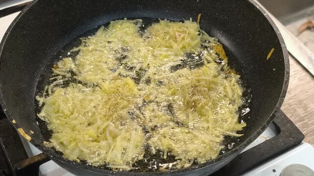 Large grated potato fritter cooking in a frying pan. Hot oil bubbles around the potato pancake as a golden crispy crust forms during frying. Homemade potato pancake made from coarsely grated potatoes.