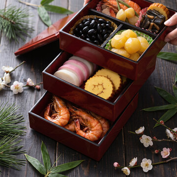 Traditional Japanese New Year osechi dishes being arranged in elegant lacquer tiered box