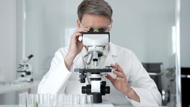 Research scientist looking through a microscope. Adjusting the focus and objective to analyze a specimen