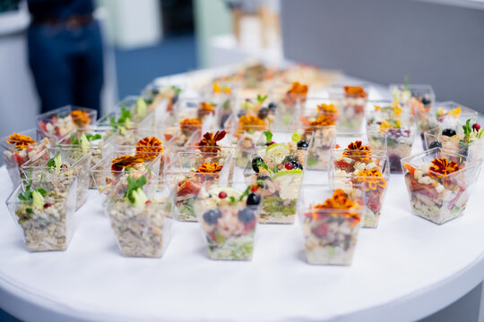 Individual salad portions in clear square cups with flower garnishes arranged for serving, presenting a catered buffet with ready prepared appetizers for guests