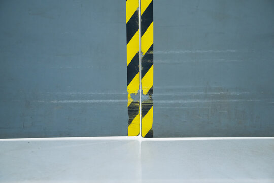 Industrial double door edges marked with worn diagonal hazard stripes above a hard floor, identifying a doorway boundary within a workplace circulation route