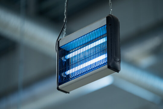 Suspended electric insect killer with twin illuminated tubes behind a protective grille, representing commercial pest control equipment for facility hygiene programs