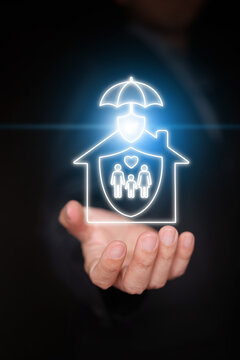 Hand holding glowing house containing family shield and sheltered by umbrella. Comprehensive property insurance, home protection, family security, and mortgage coverage. Vertical stock photo.