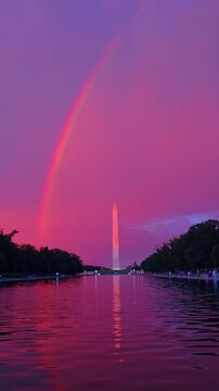 Magenta sky and rainbow above Washington Monument.. The tall capital obelisk mirrors perfectly in the calm pool water amidst deep pink clouds and a bright arc.