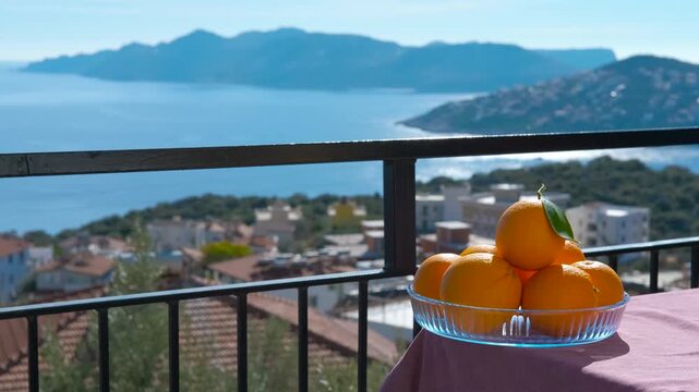 Vibrant oranges resting on balcony table. Overlooking picturesque coastal town and expansive sea under bright sunshine
