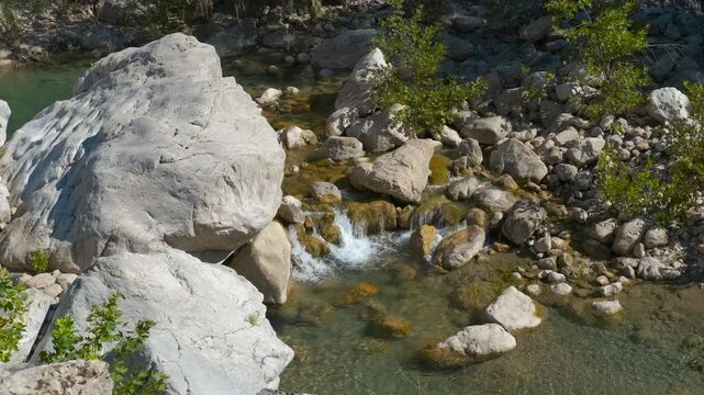 Crystal-clear stream flowing through rocky landscape. Refreshing stream water flows gracefully over rocks and pebbles, creating small cascades and highlighting the natural beauty of the landscape