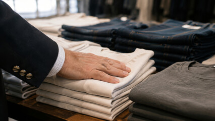 Fototapeta premium Customer touching a stack of neatly folded pants in a clothing store with jeans and shirts on display, representing retail shopping and casual fashion