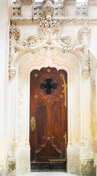 Antique ornated wooden door with metal accents framed by intricate carved stonework and neogothic decorative details on a historic building.