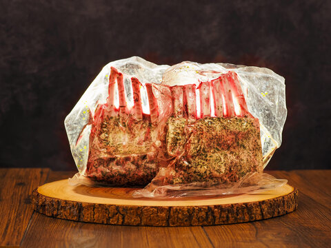 Two marinated rack of lamb in vacuum pack for extra freshness. Premium top quality lamb meat on wooden board and dark background. Butcher craft and skill. Preserving taste and flavor concept.