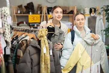 Adult woman with a teenage daughter chooses a down jacket and outerwear for the winter season and cold weather. Family shopping for clothes on sale in a store © JackF