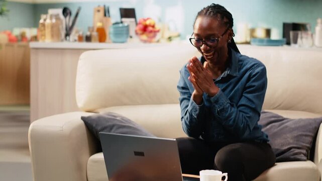 Smiling woman claps her hands overjoyed with good news, receiving promotion and career achievement at home. Uplifting ambitious person shows satisfaction, gratitude and excitement at home.