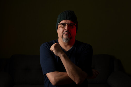 Thoughtful mature man in beanie sitting in dramatic low key light