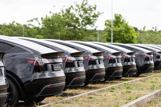Row of new black Tesla Model Y cars parked rear view at delivery lot