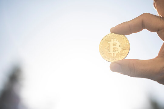 Gold bitcoin coin held between two fingers against a high key sky