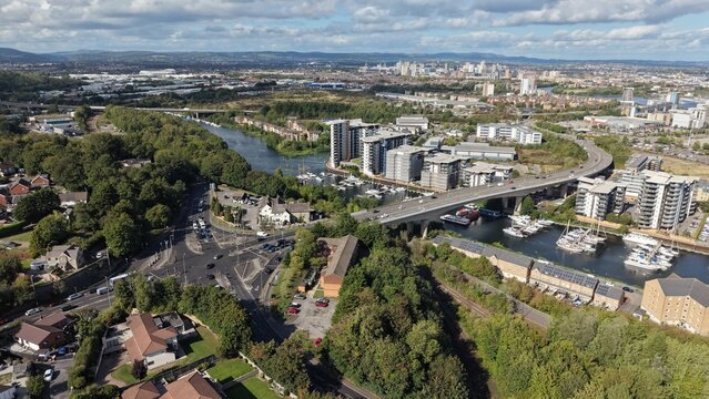 Aerial view of Cardiff, Wales, showing a major road bridge crossing a waterway, residential buildings, marina with boats and green urban landscape under a partly cloudy sky.