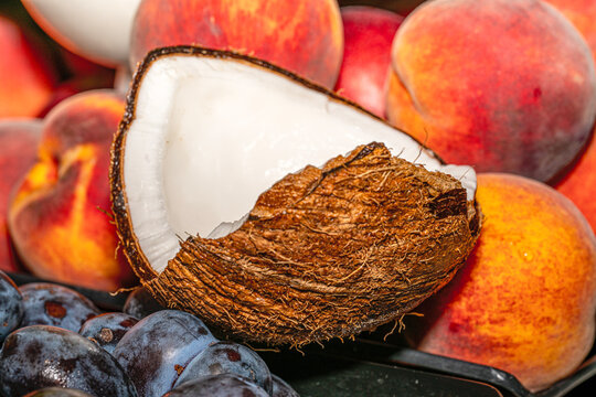 Fresh summer fruit composition featuring ripe peaches, purple plums, and a cracked open coconut.