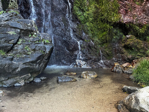 Refreshing waterfall cascading over dark rugged rocks into a clear shallow pool surrounded by lush greenery