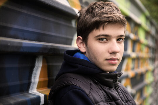 Portrait of a teenage boy leaning against metal shutters with graffiti