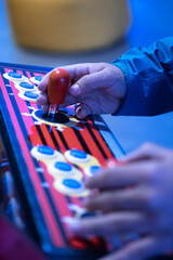 Hands on an arcade joystick and buttons under blue light, close-up © janvaneyck