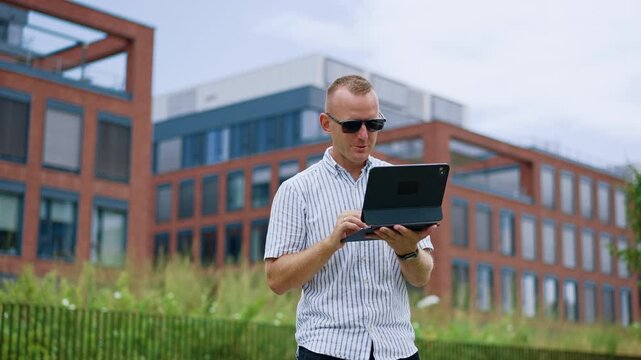The individual wearing sunglasses interacts with a touch screen outside an office block.