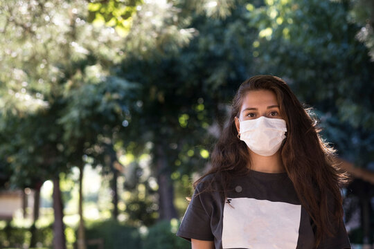 Young woman wearing a surgical mask standing under trees in a park