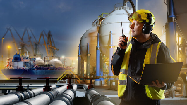 LNG terminal. Engineer coordinates liquefied natural gas operations with a radio and laptop, monitoring storage tanks, pipelines and tanker loading at a marine export facility.