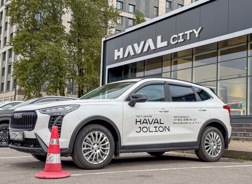 White Haval Jolion test drive SUV car parked outdoors on asphalt street next to a modern Haval City dealership showroom glass building facade. Premium Chinese crossover automobile transport vehicle. 