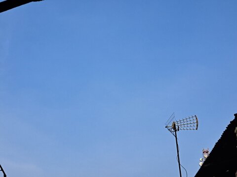 Outdoor Digital TV Antenna Mounted on House Pole Against Clear Blue Sky
