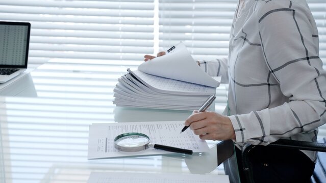 Professional woman categorizing important business documents and financial statements on an office desk. Managing a stack of files during a detailed audit