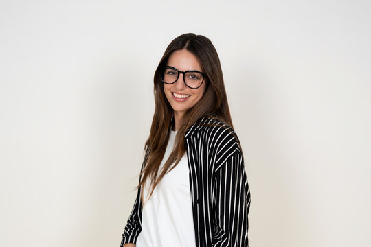 Friendly young woman smiles confidently while wearing glasses and a striped shirt in a bright studio portrait. Casual, approachable look conveying professionalism, warmth and modern style for lifestyl