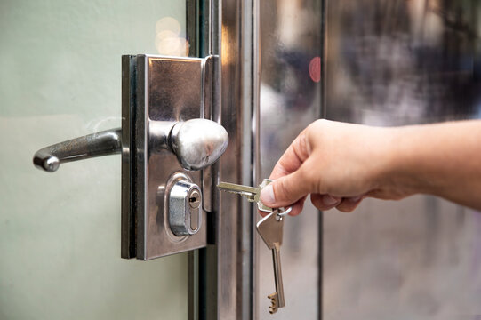 Opening a door with a key. Human hand inserting a metal key into the lock cylinder of a glass door