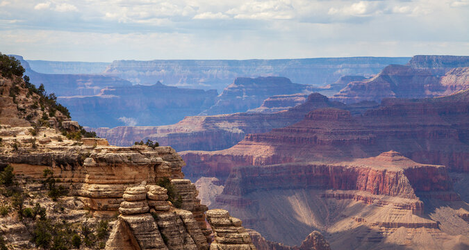 Layered Grand Canyon cliffs and mesas displaying colorful sedimentary rock strata beneath clouds in a broad Arizona national park landscape