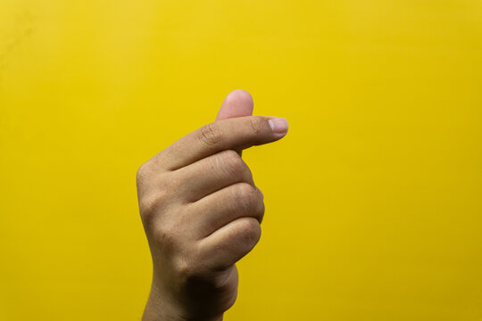 One male hand demonstrates popular finger heart gestures set against bright yellow background, Thumb intersects index digit slightly creating miniature symbols widely recognized across
