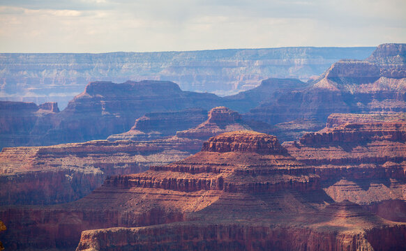 Layered Grand Canyon cliffs and mesas glowing in soft sunlight beneath a hazy blue sky, revealing vast erosion patterns and colorful geological strata in Arizona landscape