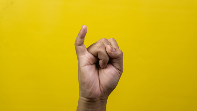 One single male hand extends pinky finger upward while remaining digits curl tightly into palm against yellow background, This distinctive gesture remains globally recognized symbolizing