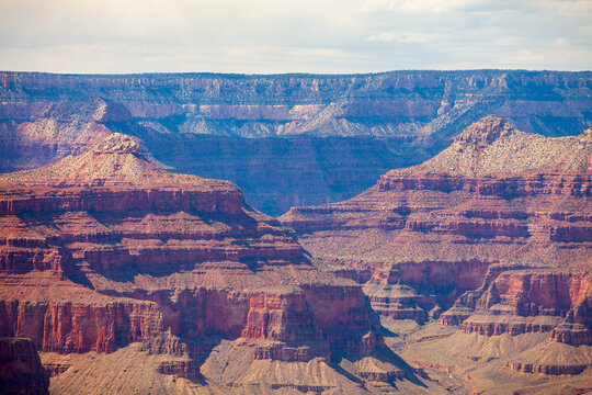 Layered Grand Canyon cliffs and deep rugged ravines illuminated by warm sunlight beneath cloudy skies, expansive geological landscape in northern Arizona