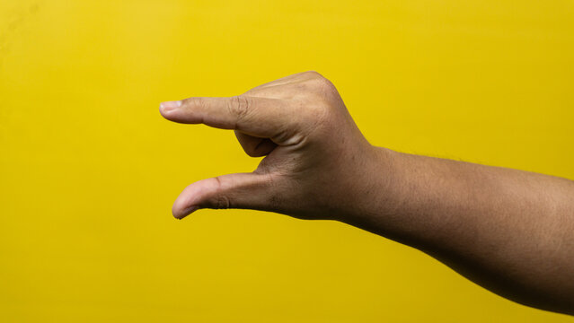 A male hand is shown from a side profile making a horizontal pinching gesture against a solid yellow background, The thumb and index finger are held slightly apart as if measuring