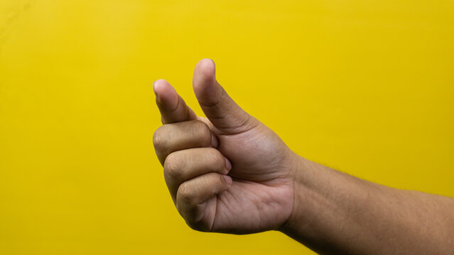 A close view of a male hand with the thumb and middle finger pressed together as if snapping or holding a thin item against a yellow background, The remaining digits are gently curled