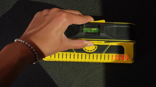 Video of a woman's hand holding a stud finder to check for wires in the wall, close-up DIY home renovation and safety inspection