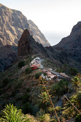 The rock spire above Masca stands sharp against the hazy mouth of the gorge. Remote mountain scenery for travel escape and off grid living storytelling. © Oksana