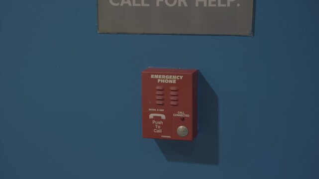 A stark, high-contrast shot of a bright red emergency phone mounted on a solid blue wall with a prominent safety warning sign positioned directly above it. 