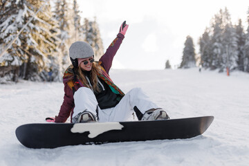 Fototapeta premium Girl snowboarding on a snowy slope while wearing a helmet and colorful jacket during a sunny day in a winter resort