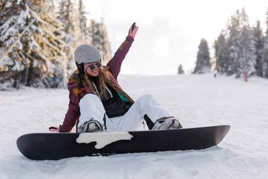 Girl snowboarding on a snowy slope while wearing a helmet and colorful jacket during a sunny day in a winter resort