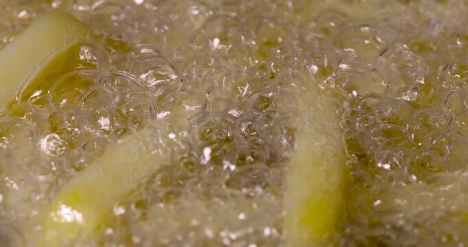 Yellow french fries frying in hot bubbling oil, homemade sliced potato french fries cooking in boiling grease liquid inside skillet