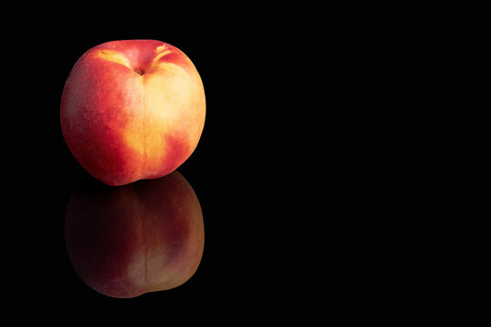 A single fresh nectarine with a vibrant red and yellow skin isolated on a deep black background