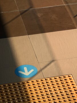 Directional arrow sign on floor next to yellow tactile paving blocks for visually impaired, warm golden hour sunlight falling on ground