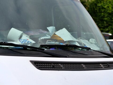 Close-up of a cluttered delivery van dashboard filled with loose documents, tissues, and trash behind glass.
