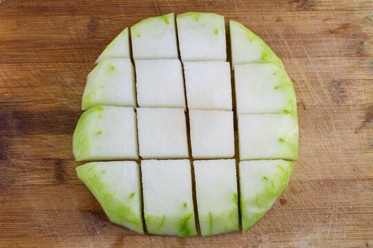 Raw sliced winter melon cut into even pieces, laid on a wooden cutting board for food preparation.