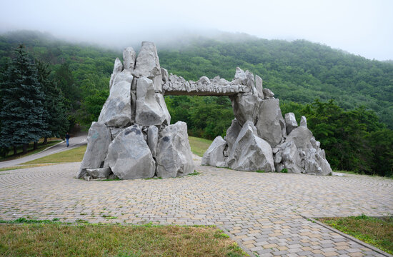 Large stone arch monument in a public park agaist Mashuk Mountain, Pyatigorsk, Russia. Gray rock structure with foggy green forest background