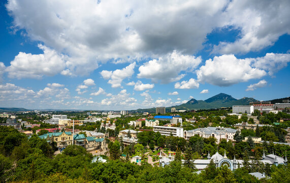 Aerial view of a green city in a mountain valley during summer, Pyatigorsk, Russia. Urban landscape with trees, and a prominent peak in the background. Copy space in the blue sky